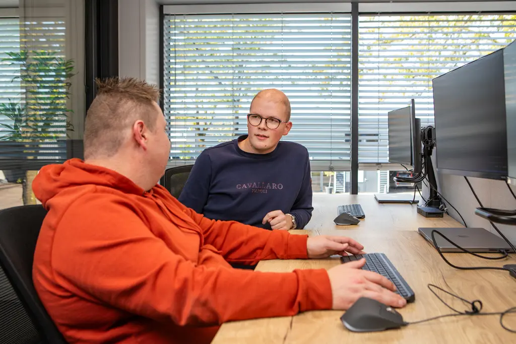 Twee developers van Orange Bits overleggen aan een bureau met beeldscherm